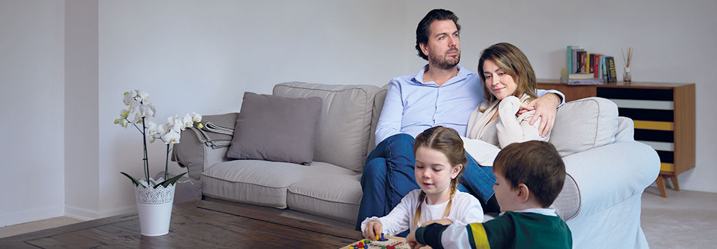 Familie sitzt unbesorgt auf Couch, Kinder spielen